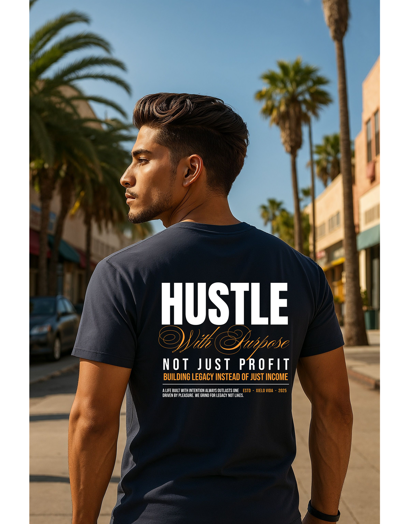 Man walking outdoors on a sunny street lined with palm trees, wearing a navy premium t-shirt featuring a bold back print that reads ‘Hustle With Purpose — Not Just Profit, Building Legacy Instead of Just Income’ in white and gold lettering by Xielo Vida.