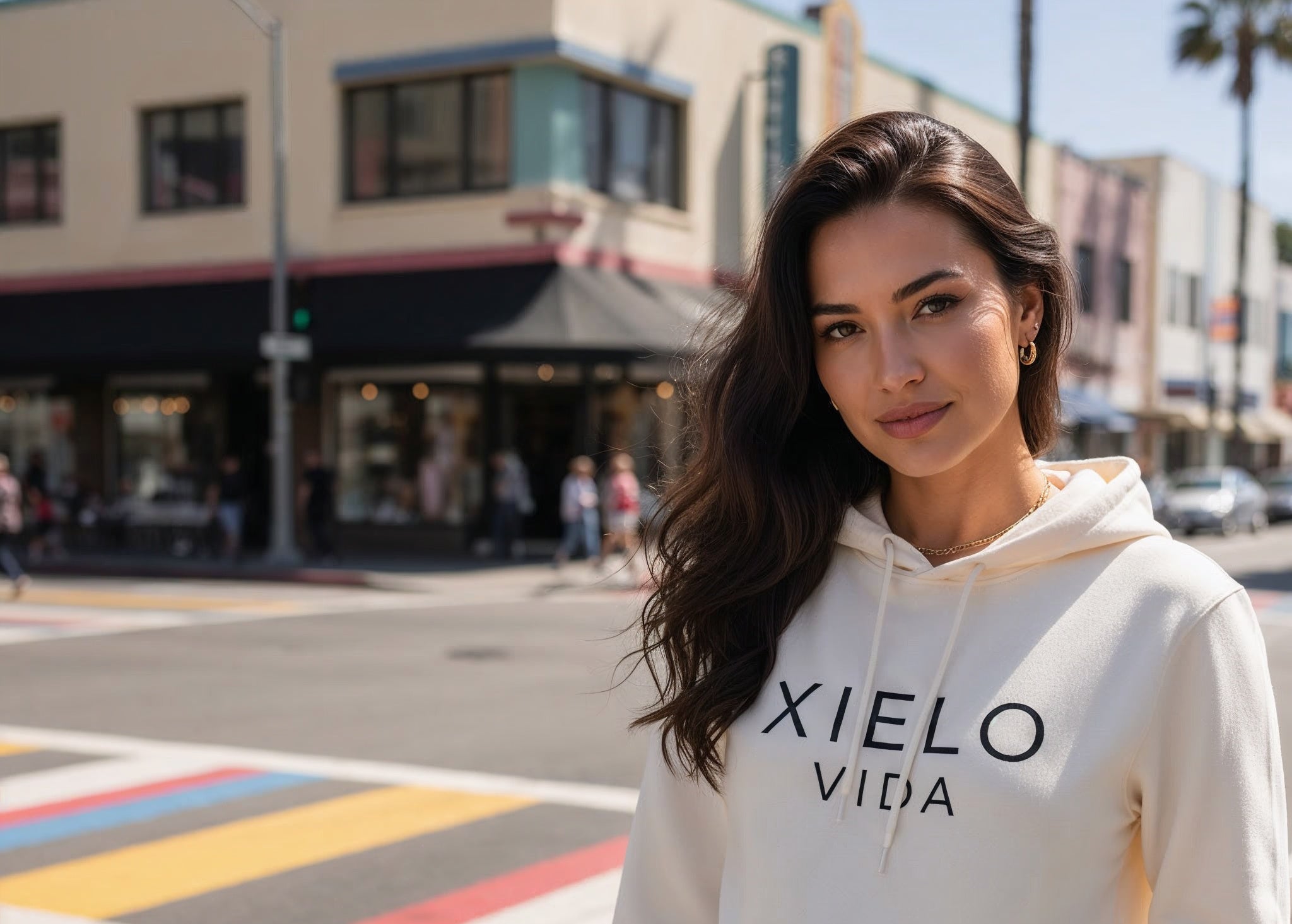 Woman wearing a white hoodie with 'XIELO VIDA' text on a city street.